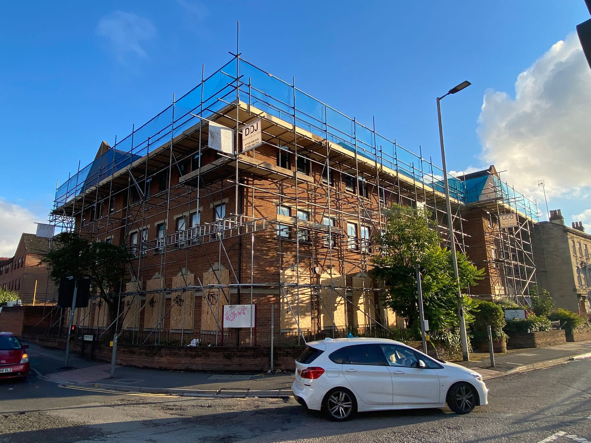 A red-brick Victorian corner block scaffolded across two elevations, seen from the far side of the street