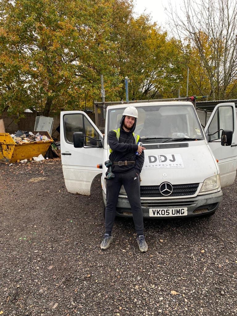 A DDJ scaffolder in a helmet and harness beside the branded DDJ Scaffolding van