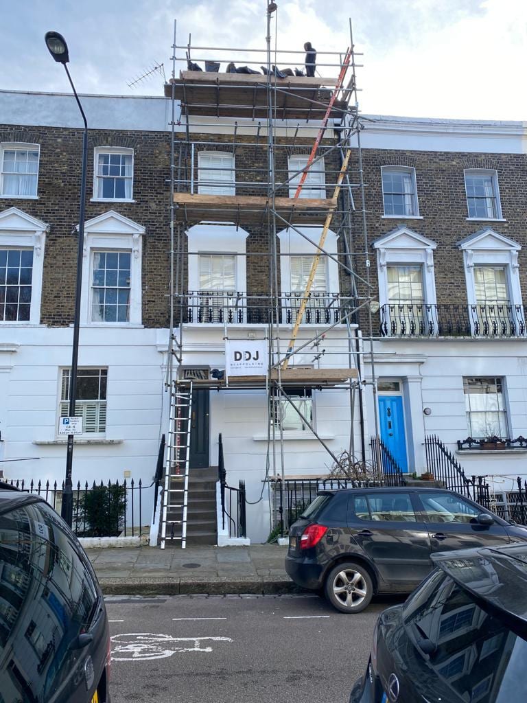Scaffolding rising the full height of a Georgian terraced house, with a scaffolder working on the top lift