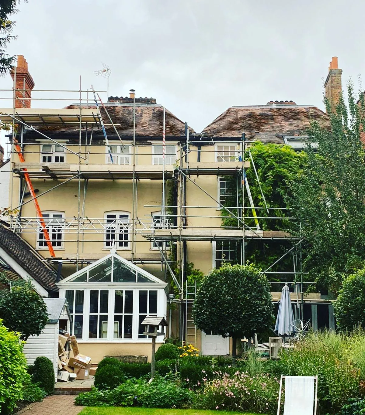 Several lifts of scaffolding across the rear elevation of a large period house, stepped around a conservatory