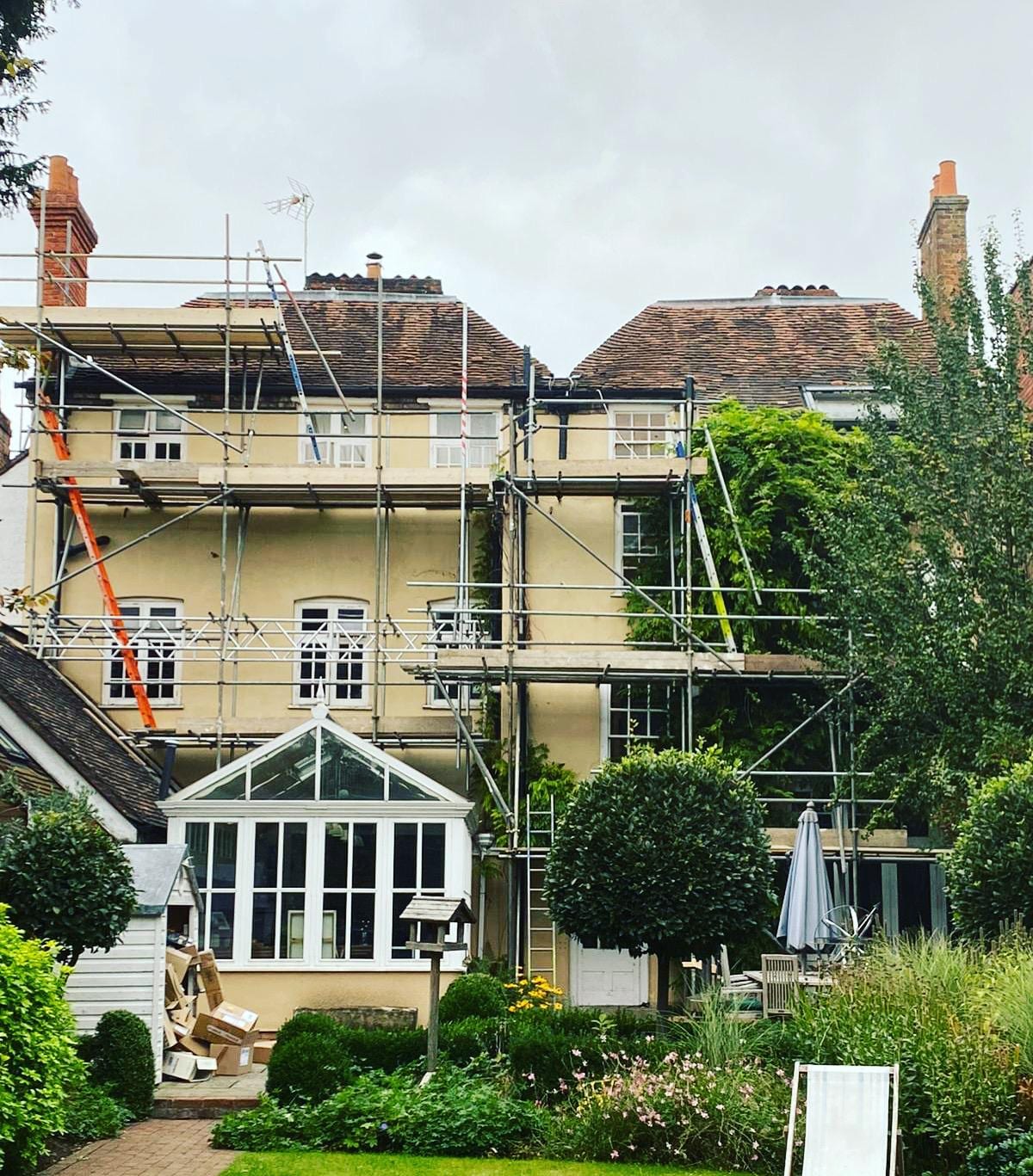 Several lifts of scaffolding across the rear elevation of a large period house, stepped around a conservatory