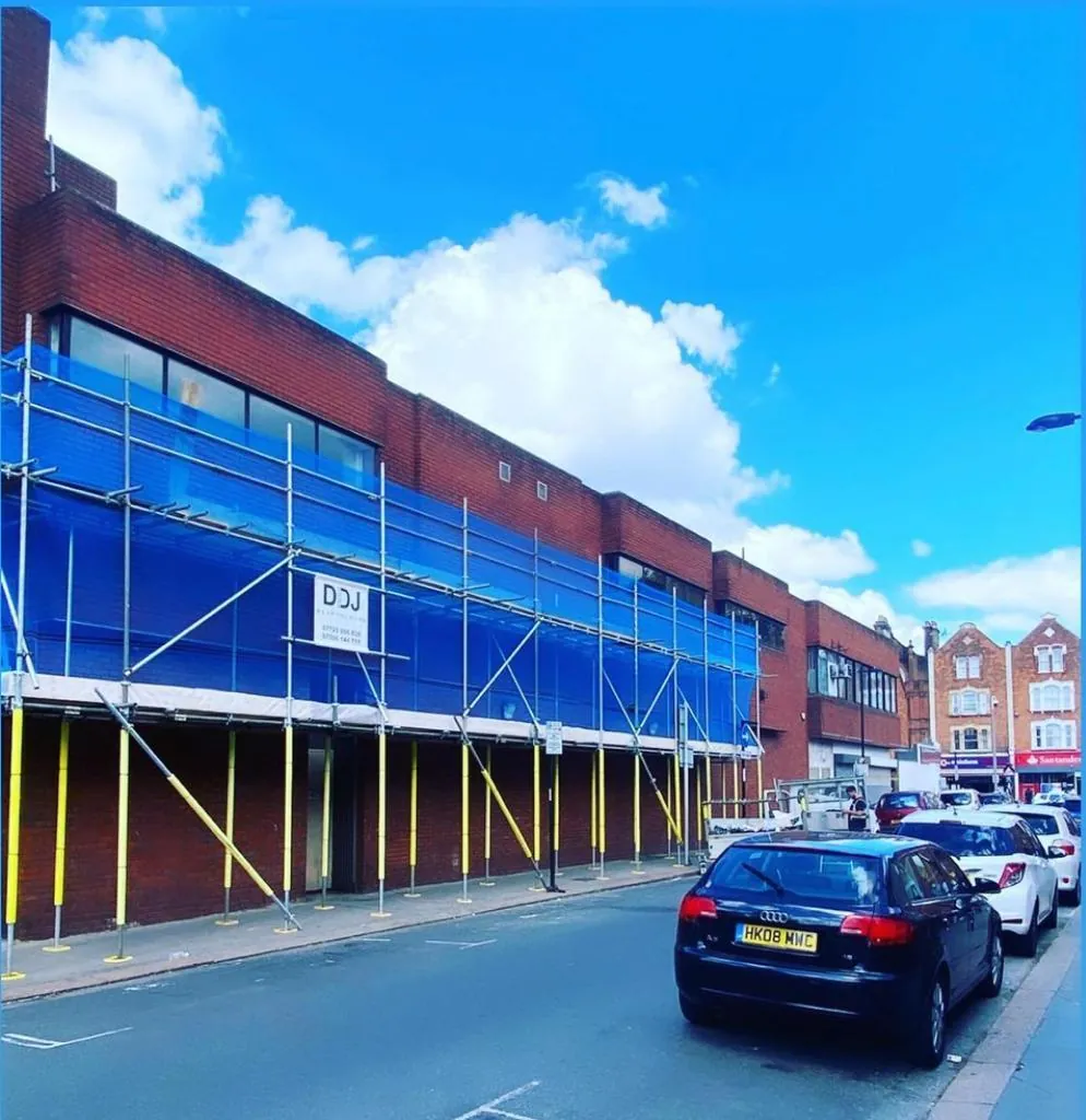 A long scaffold run along the glazed frontage of a retail parade beside a main road