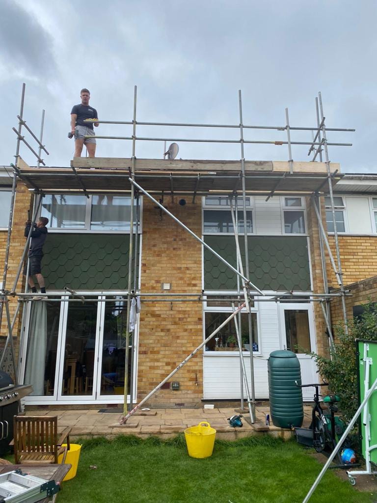 Two DDJ scaffolders building a scaffold across the rear of a house, one on the top lift and one climbing