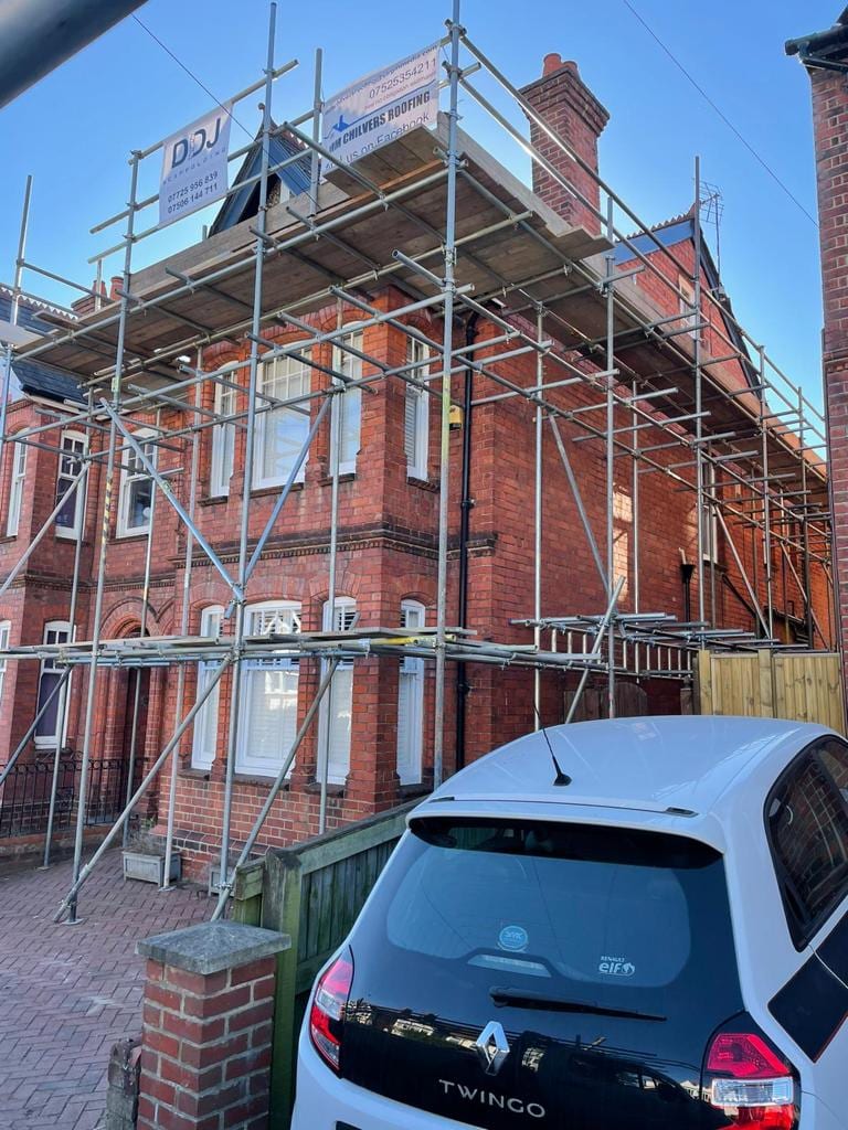 Scaffolding up the front of a brick house reaching above the eaves to roof height