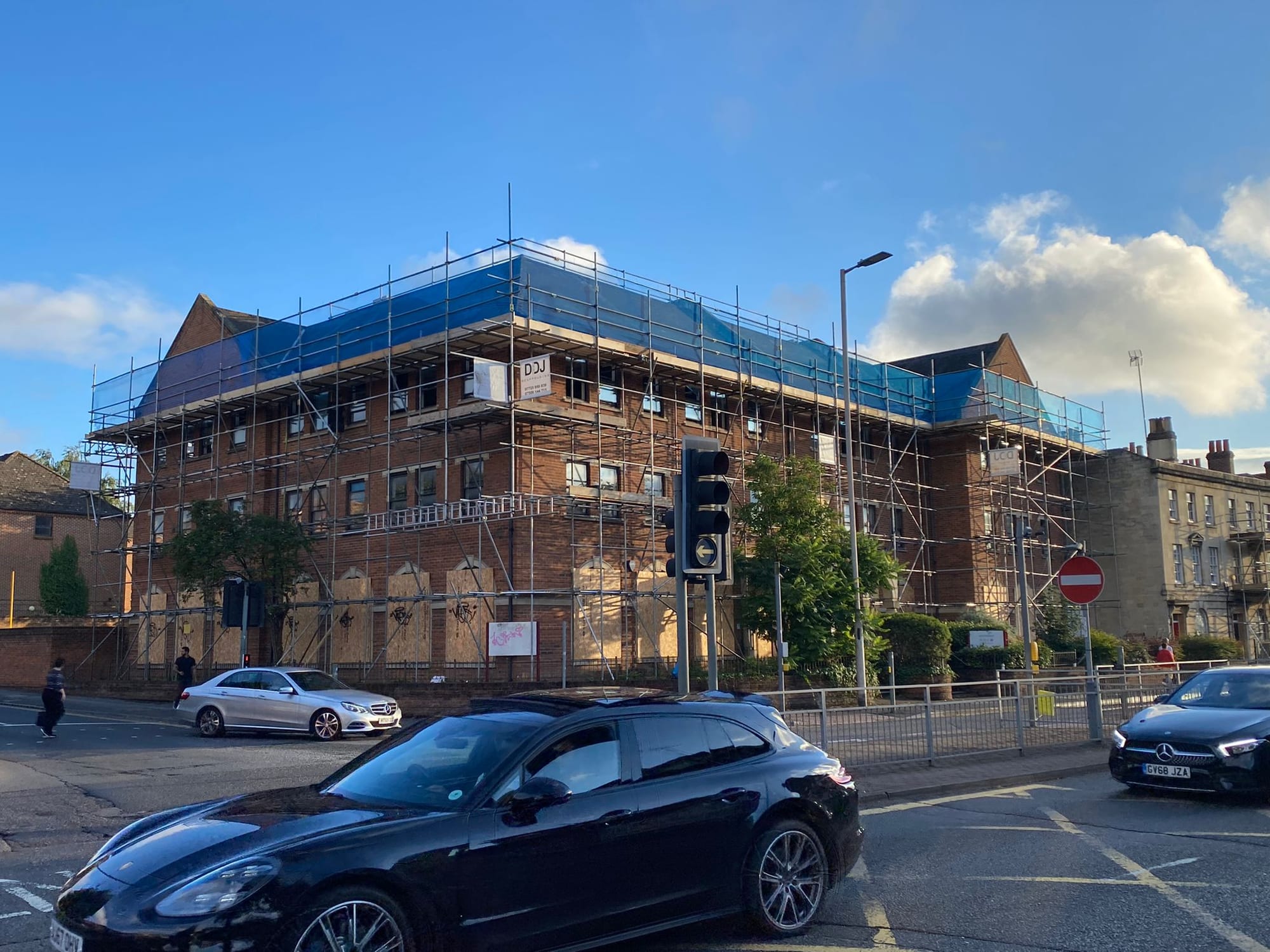 A large Victorian corner block scaffolded to roof level and sheeted, on a road junction with traffic passing