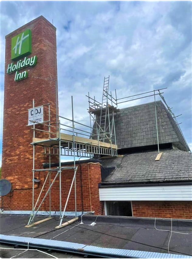 A scaffold tower and boarded platform built at roof level against a tall brick signage tower