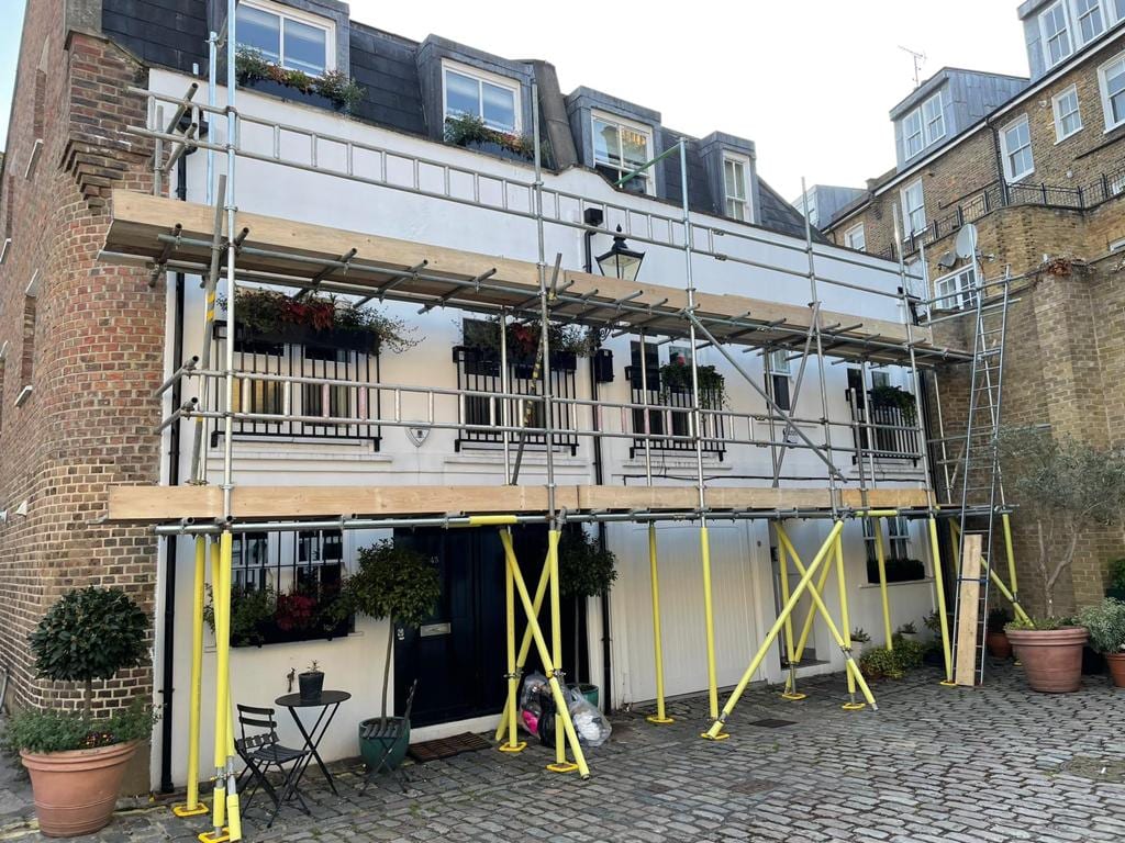 A boarded scaffold lift across the frontage of a white-fronted building on a cobbled mews