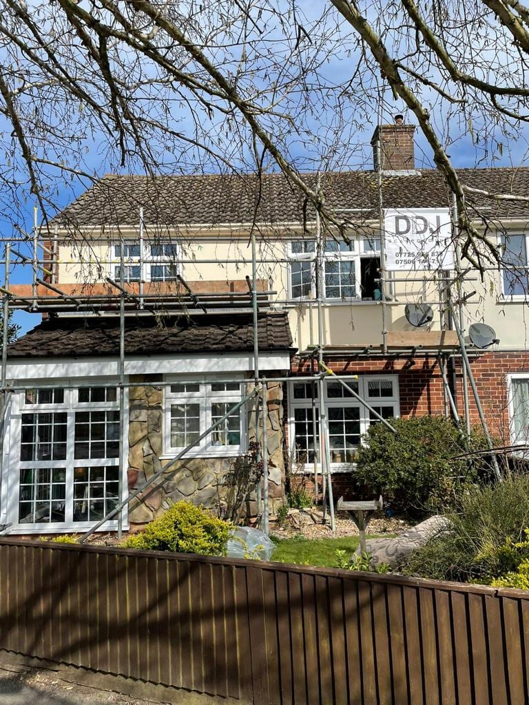 Scaffolding across the rear of a white rendered house carrying a DDJ Scaffolding banner, seen through bare branches