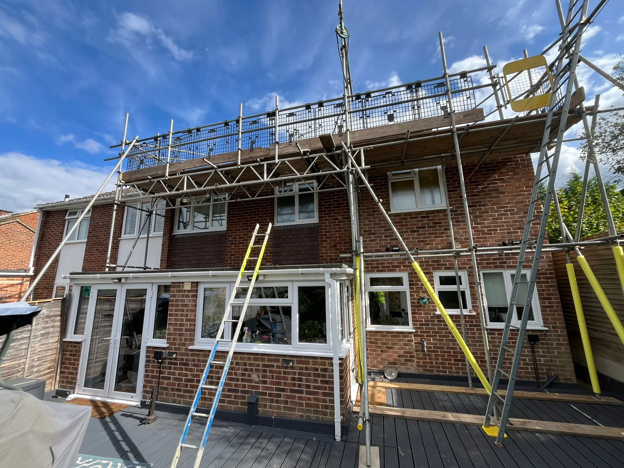 Scaffolding across the back of a brick house in Bracknell, with a boarded platform and mesh edge protection at roof level