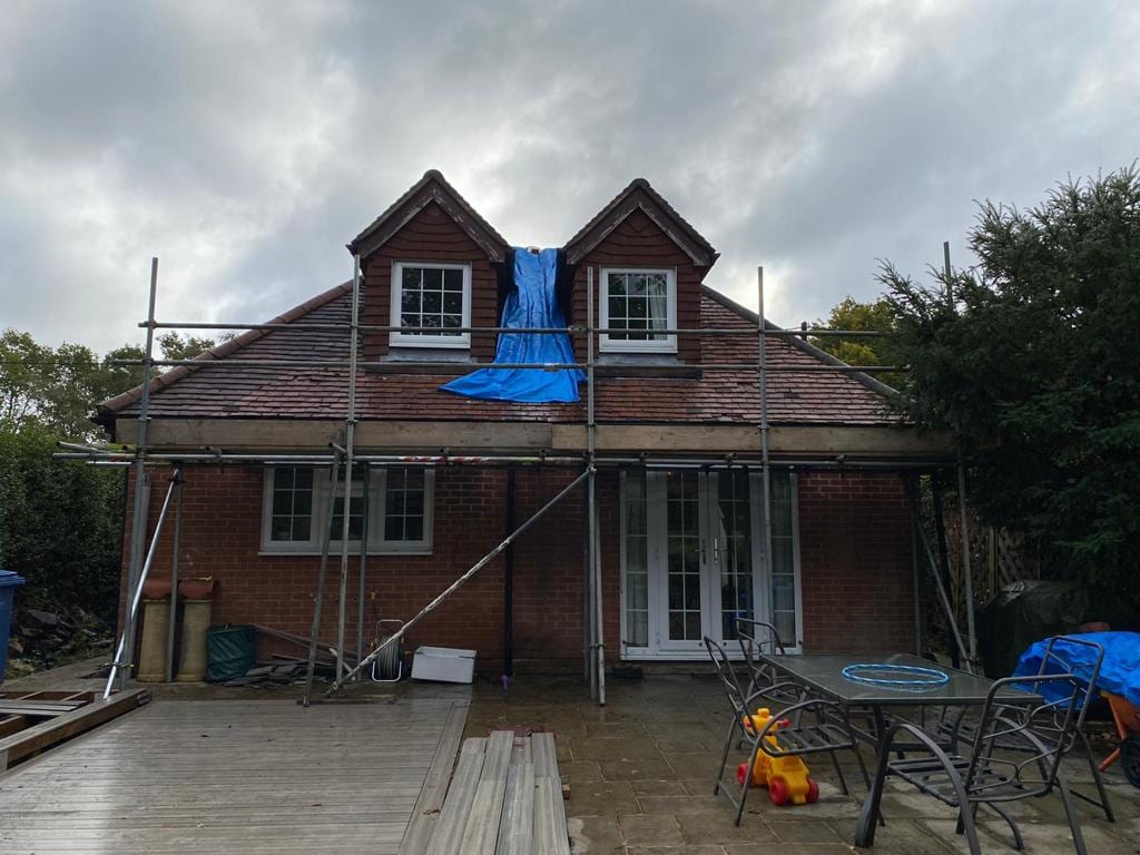Scaffolding across the rear of a house with two dormers, a weather sheet draped over the roof between them