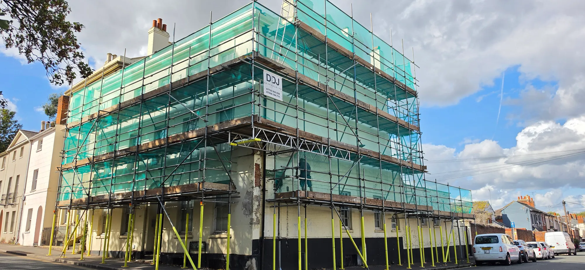 A three-storey period townhouse on a street corner, scaffolded and wrapped in green debris netting