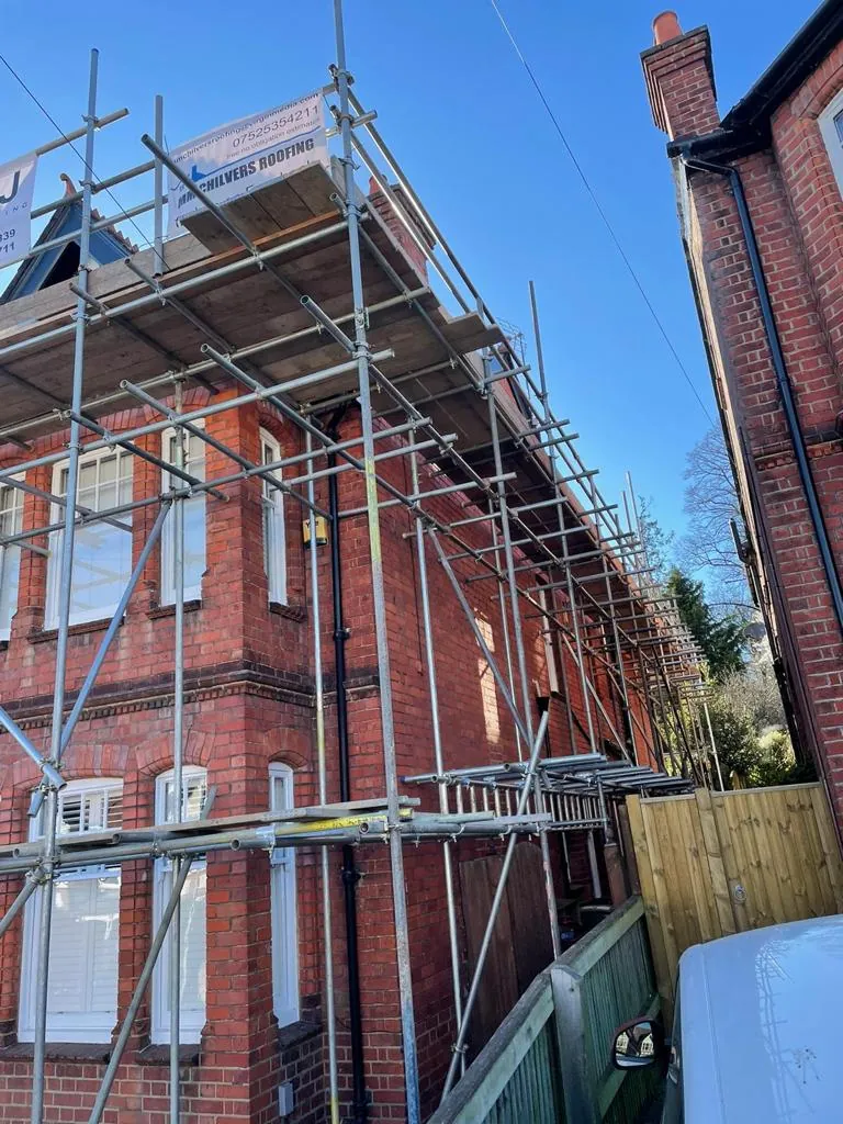 Scaffolding rising around the corner of a Victorian brick house, boarded and guarded at eaves level