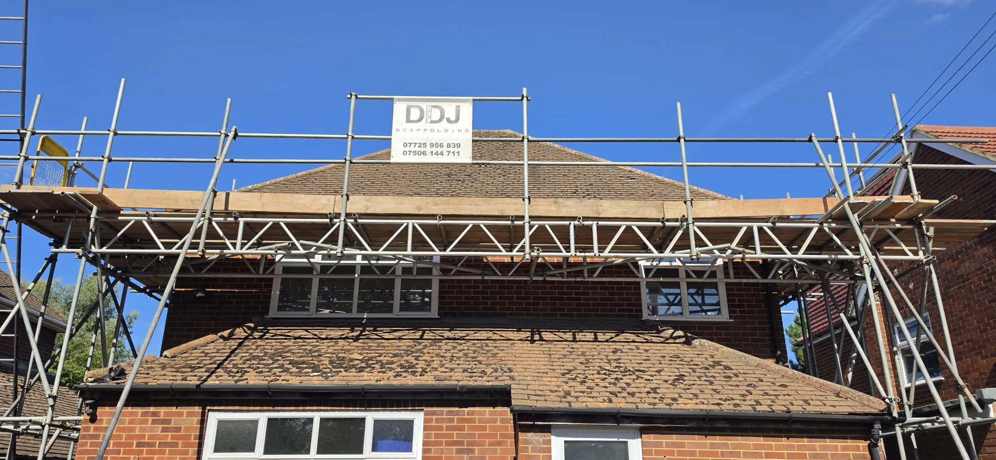 Scaffolding up to the roofline of a brick house, with a DDJ Scaffolding sign on the top lift