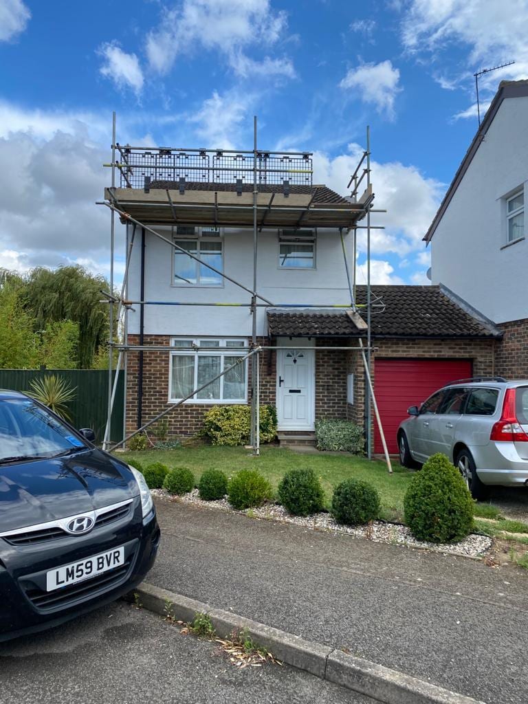 Scaffolding up the front of a semi-detached house, boarded at first-lift height with a guardrail
