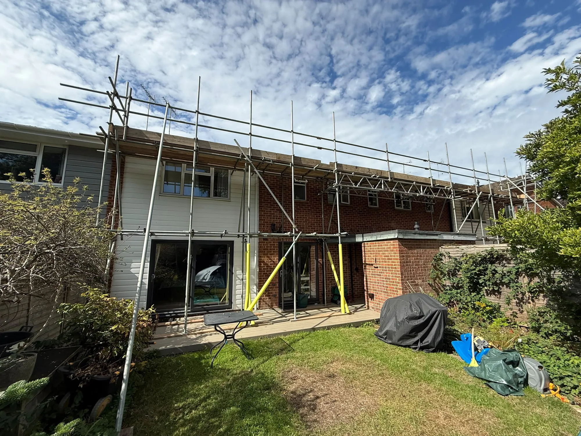 Scaffolding along the back of a two-storey house, seen across the rear garden