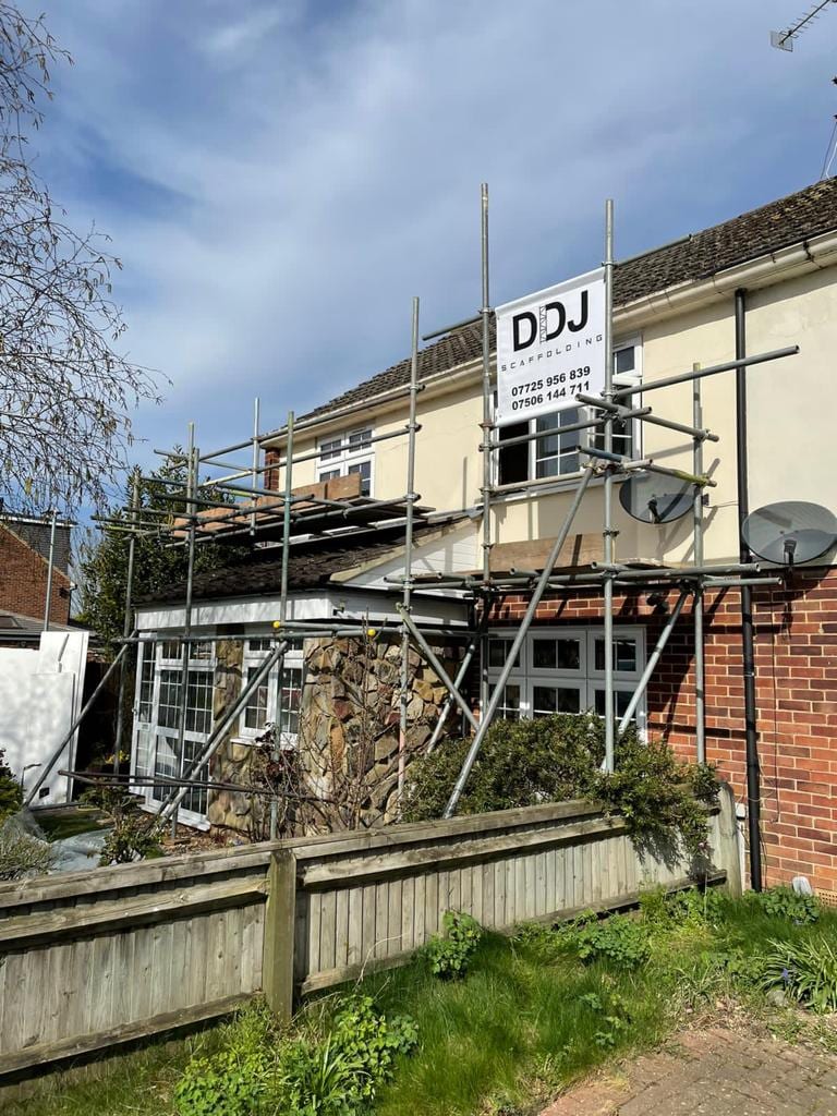 Scaffolding along the rear of a white rendered house above a stone-clad conservatory, carrying a DDJ Scaffolding board