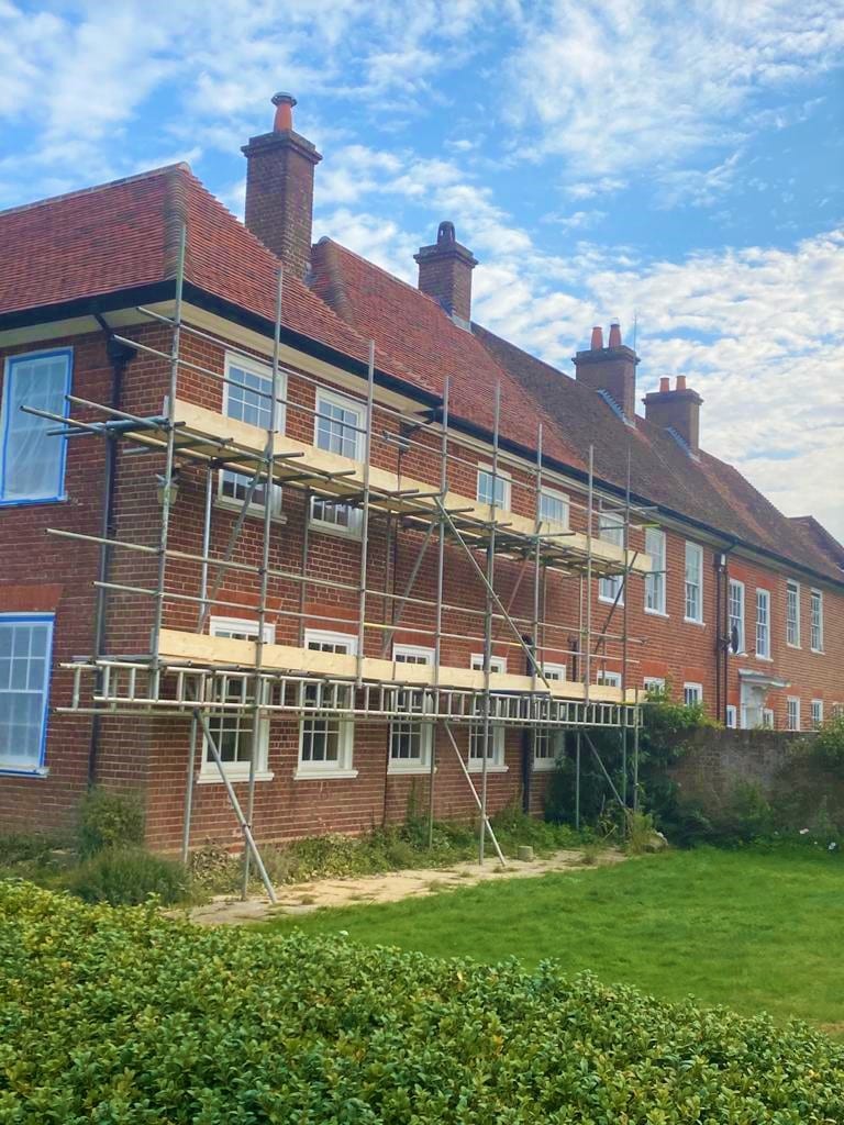 A single lift of scaffolding running the length of a row of brick cottages beneath tiled roofs and chimney stacks