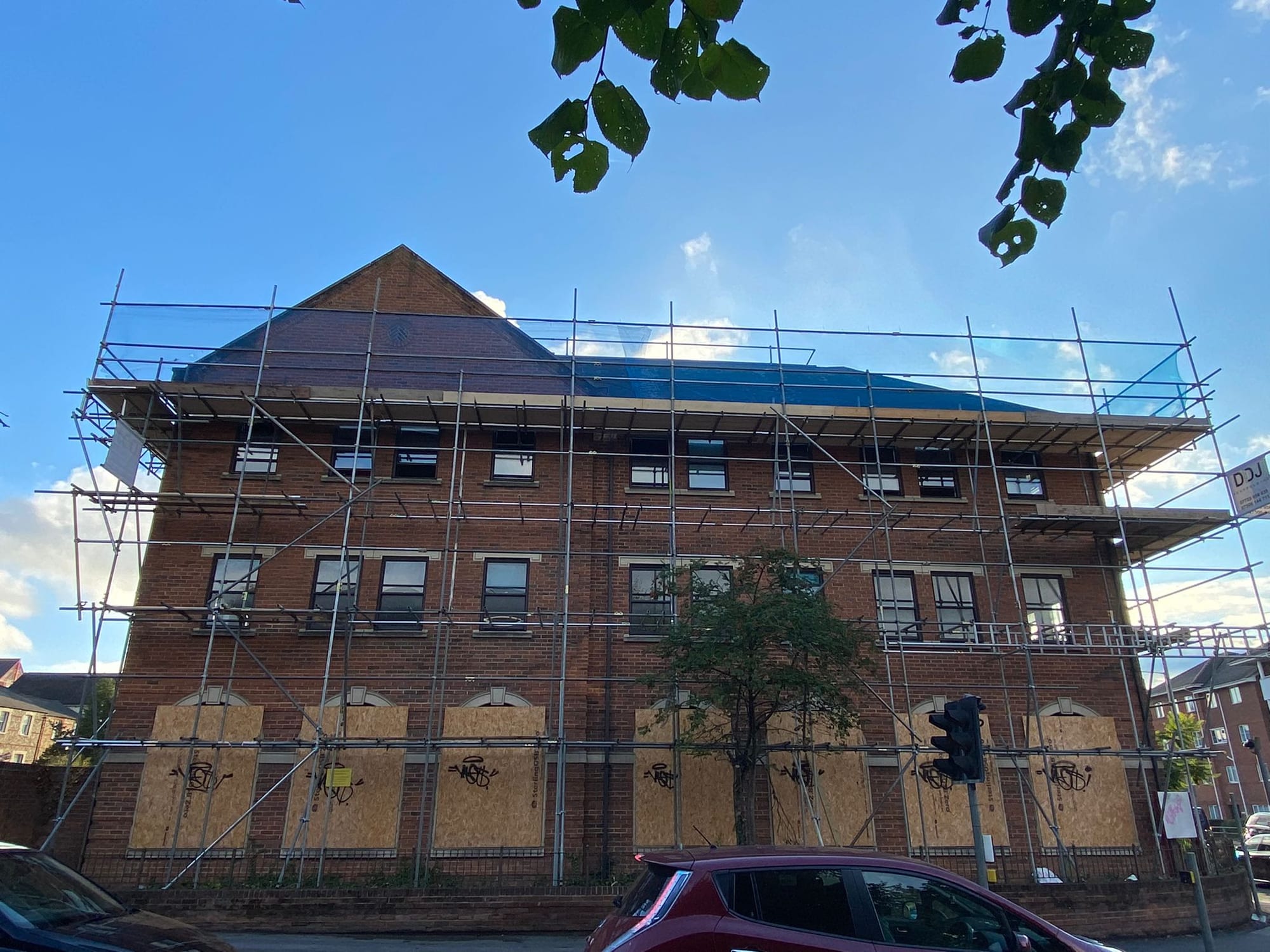 The gable end of a red-brick Victorian block scaffolded to roof height, three boarded lifts running the full width of the elevation