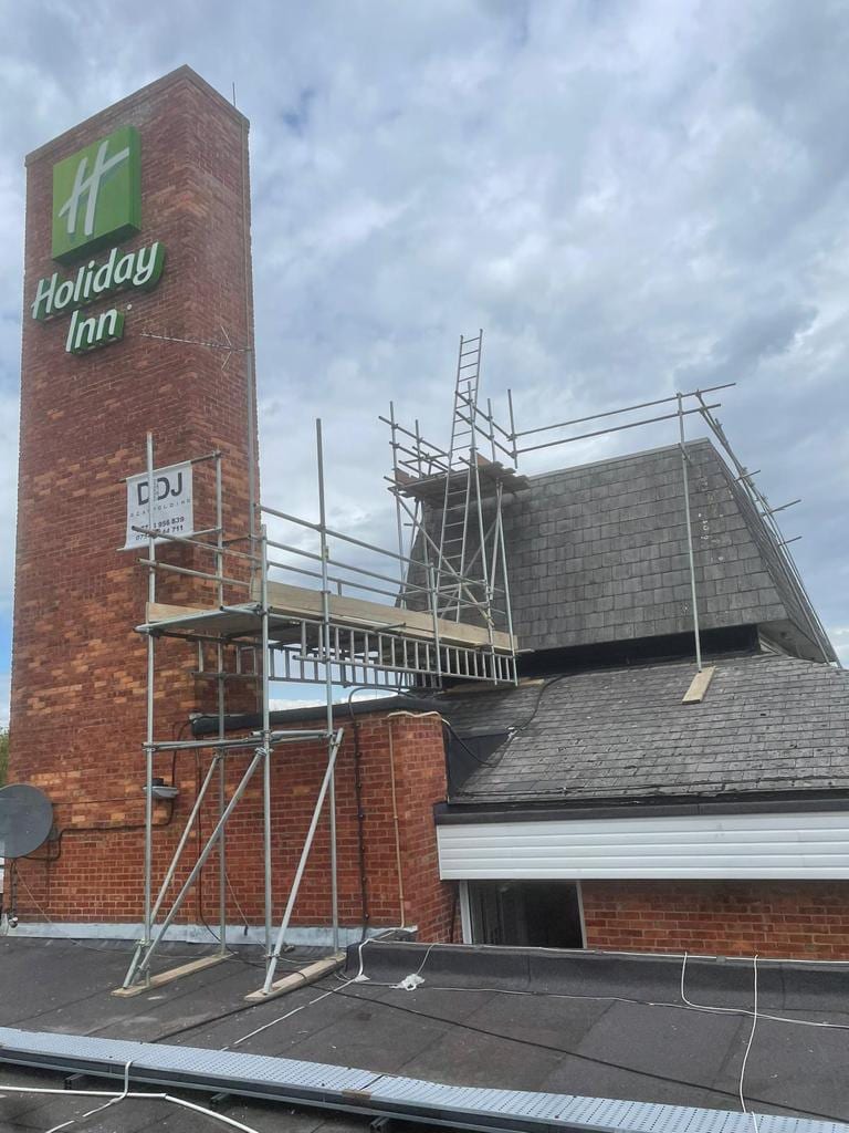 Scaffold beams spanning a flat commercial roof, boarded out and guardrailed, with plant and ductwork alongside